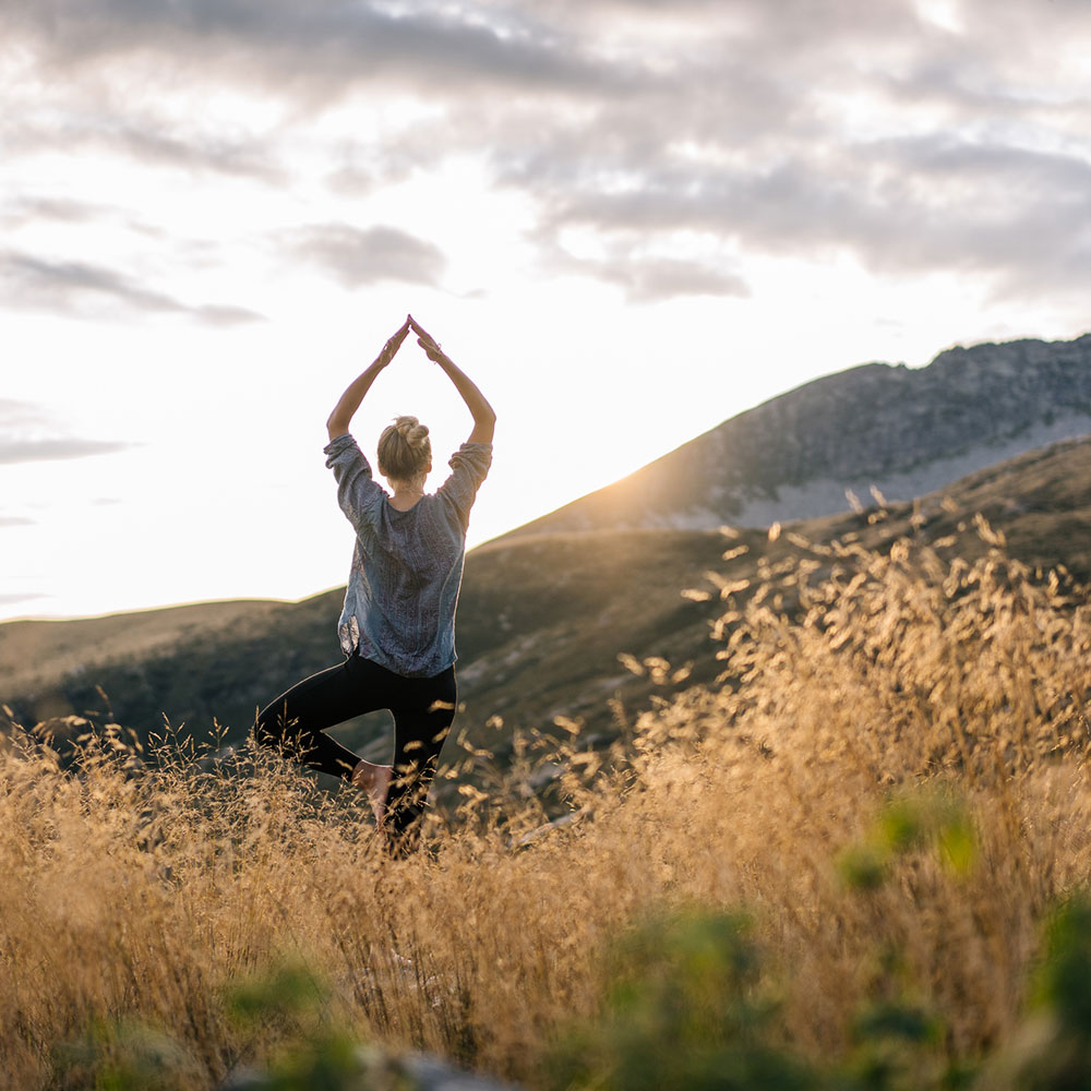 Young woman preforms yoga in mountains in morning light