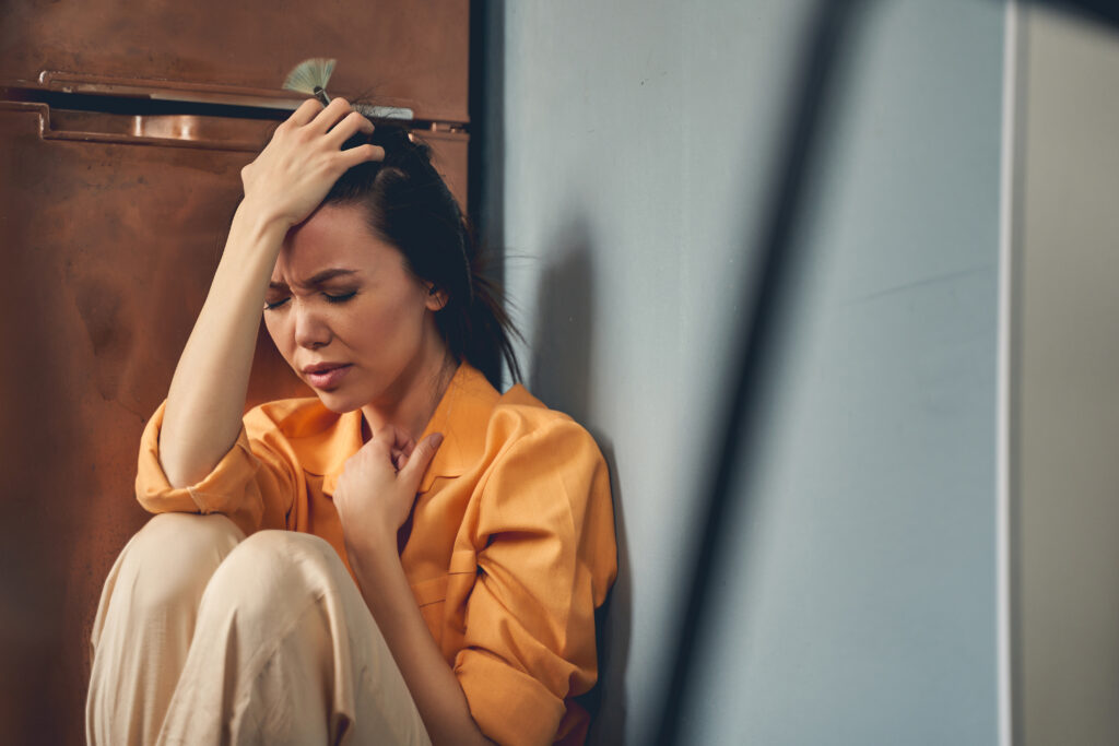 Upset woman placing hand on head and closing eyes while suffering from pain