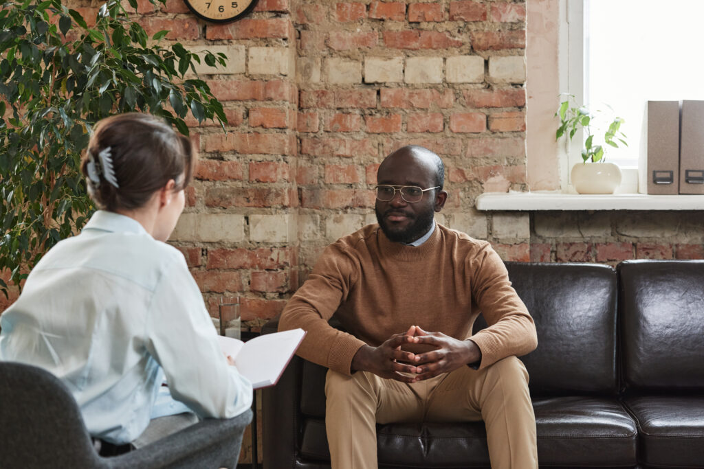 Psychologist with organizer asking black patient in glasses at therapy while analyzing his problems
