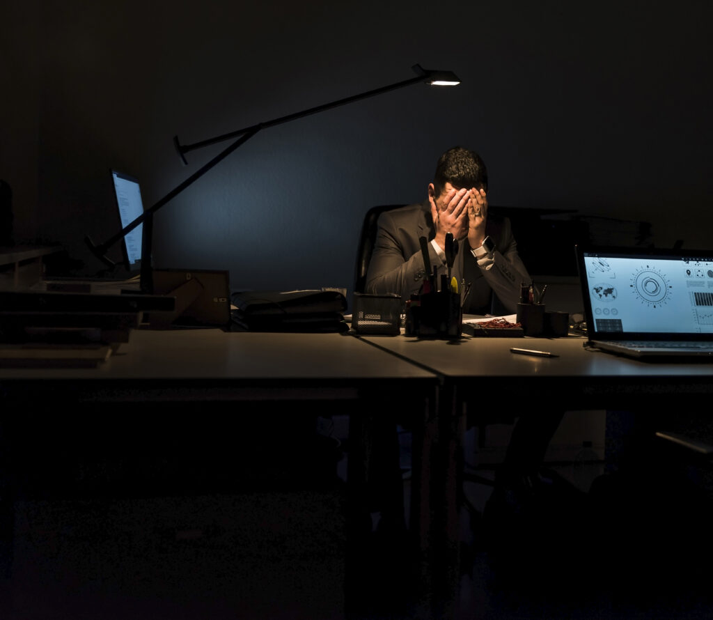 Overstressed businessman sitting at his desk in the dark